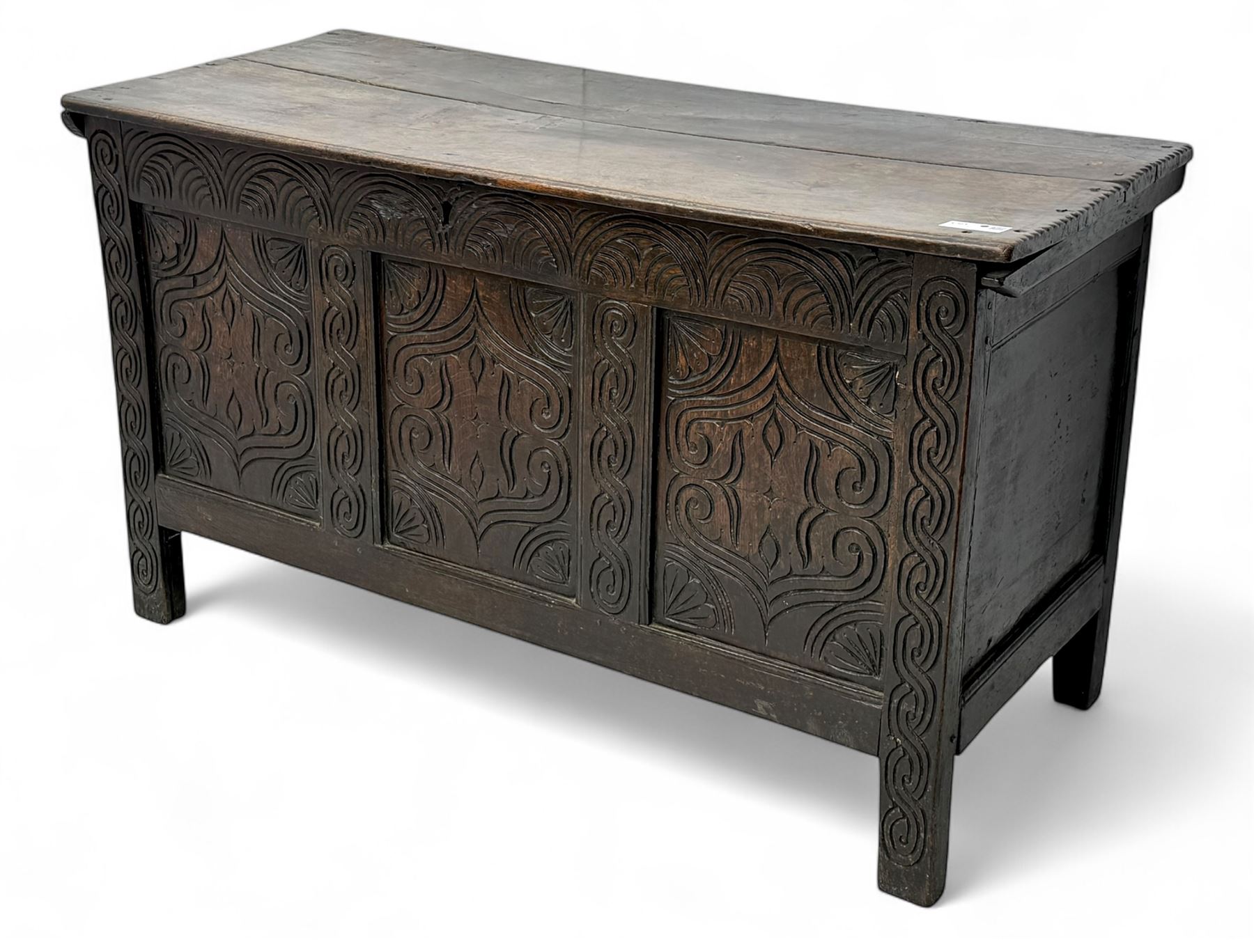 English carved oak coffer, hinged rectangular lid with indented side edges, internal candle-box, front with three-panel front with decorative carvings, raised on stile feet, circa 1700