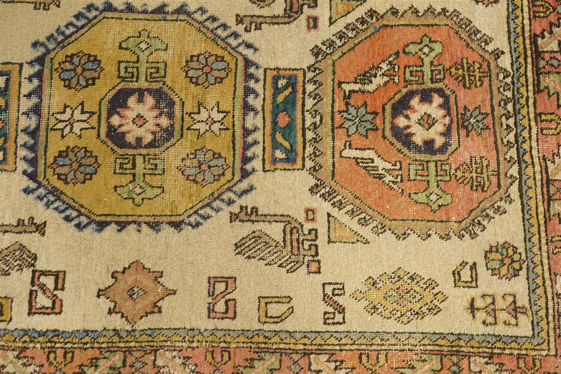 Two Caucasian designed rugs comprising a flatweave and hand-knotted rug, Caucasian design flatweave, cream ground with three large blue geometric medallions surrounded by stylised birds and geometric motifs, enclosed by repeating geometric border, fringed ends, H176cm, W102cm; hand-knotted Caucasian rug, ivory ground with three polychrome octagonal medallions surrounded by stylised animals, flowerheads and geometric motifs, enclosed by salmon pink geometric border, fringed ends, H163cm, W106cm