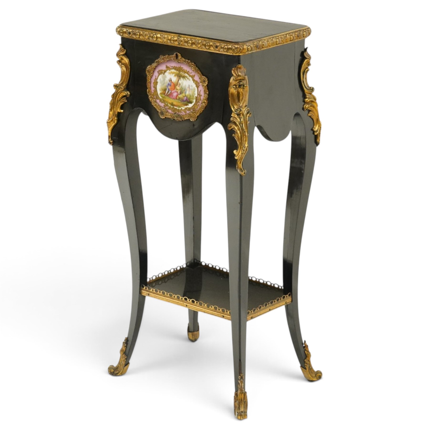 Early 20th century French ebonised sewing or work table, rectangular hinged top with foliate moulded gilt metal edge, enclosing upholstered interior, over a central Sevres style porcelain plaque depicting a courting scene, raised on cabriole supports with gilt metal carotuche and acanthus knee mounts, united by undertier with brass gallery terminating to gilt metal scroll feet