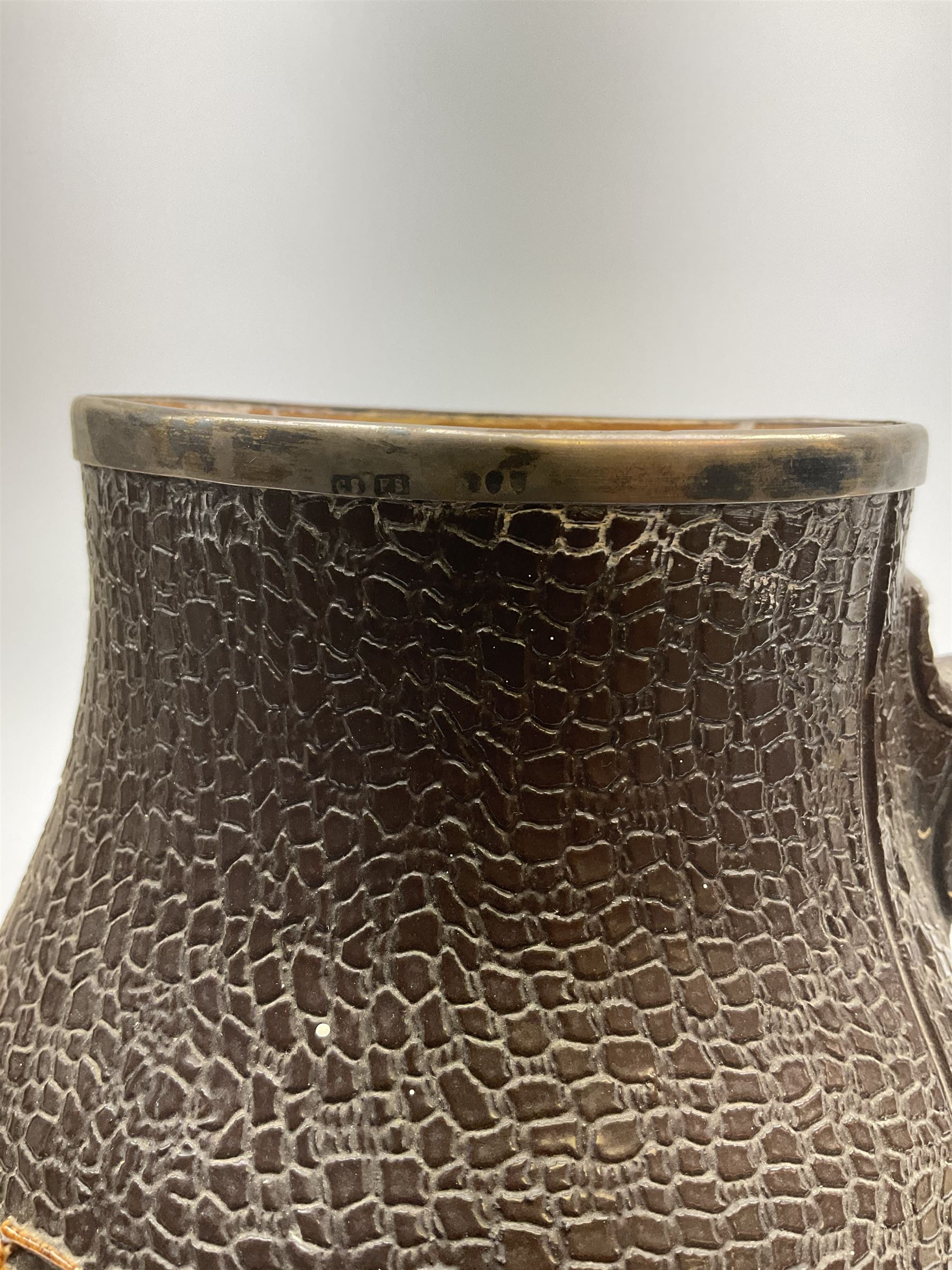 A Doulton Lambeth stoneware jug, with silver mounted collar, hallmarks rubbed, maker's mark probably Cornelius Desormeaux Saunders & James Francis Hollings (Frank) Shepherd, the leather effect body titled 'Drinke Faire Don't Sware', with impressed marks beneath including 'Manufactured for Sidney W Allen 39 White Rock Hastings', H18.5cm. 