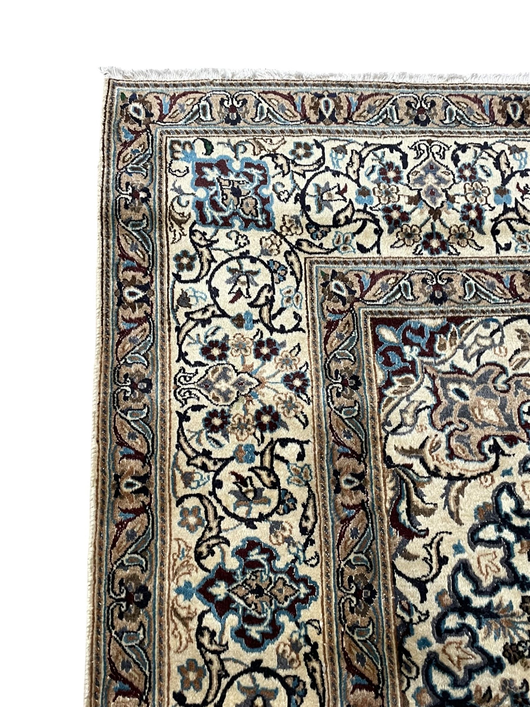 Persian Kashan ivory ground carpet, central rosette medallion surrounded by swirling leafy branches and floral sprays, the main border with scrolling pattern interspersed with floral motifs, within guard stripes 