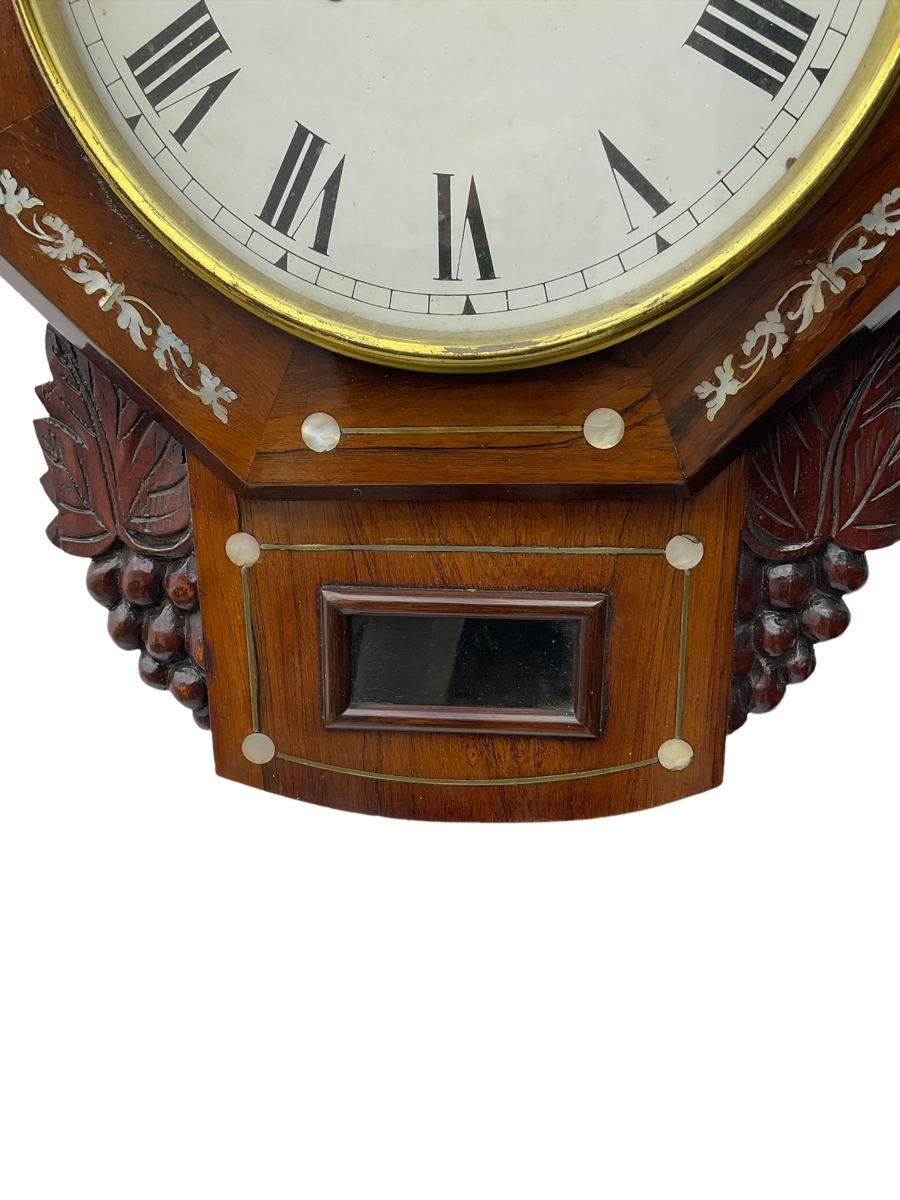 American - late 19th century 8-day mahogany drop dial wall clock, with a hexagonal dial bezel inlaid with mother of pearl, pendulum box with a rectangular viewing glass flanked by carved representations of grape vines, with a painted dial with roman numerals, minute track and steel spade hands within a spun brass bezel, eight day striking movement striking the hours on a gong.   With pendulum & key.