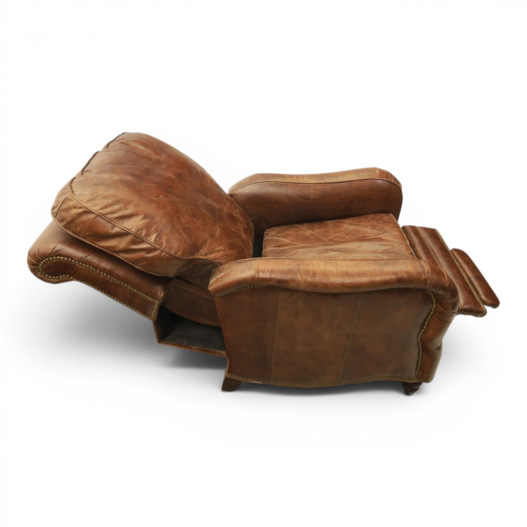 Art Deco style brown leather reclining armchair, scrolled arms with brass studded trim, reclining foot rest and back, fixed back and loose seat cushion,