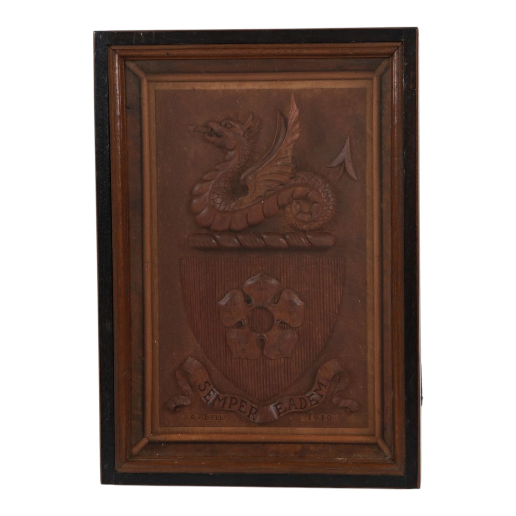 Early 20th century relief carved oak crest depicting shield with central five point flower head, surmounted by a recumbent dragon, above a banner inscribed with the Latin motto 'Semper Eadem' (Always the same), signed A E Bell nd dated 1910, in a glazed case, overall 35cm x 25cm
