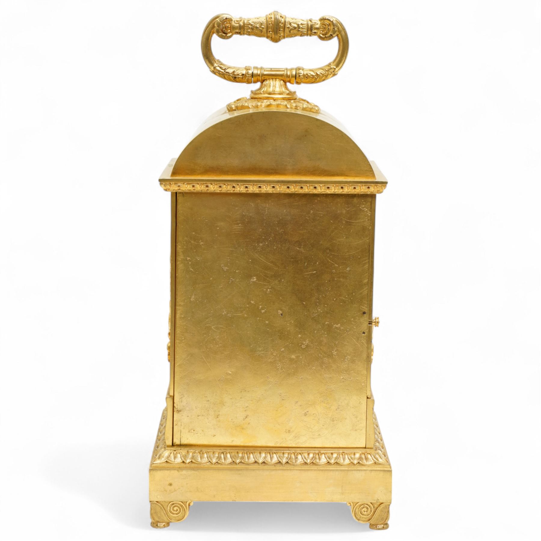 Fine Swiss ormolu 8-day early 19th century Pendule d'Officer style clock c1820,  circular double train ting-tang movement striking the quarters on a graduated pair of bells and sounding the hour on one, going train with a vertical platform lever escapement and over sprung balance, rack striking, with visible hour and quarter strike work to the backplate, movement unsigned, convex enamel dial with Roman numerals and steel moon hands behind a glazed gilt bezel, case with a scroll cast handle to the arched top with applied rococo decoration to the tympanum, both sides of the case adorned with a military trophy of arms motif and deep frieze with foliate arcading beneath, on a rectangular plinth with decorative scroll engraved bracket feet. With Key.   