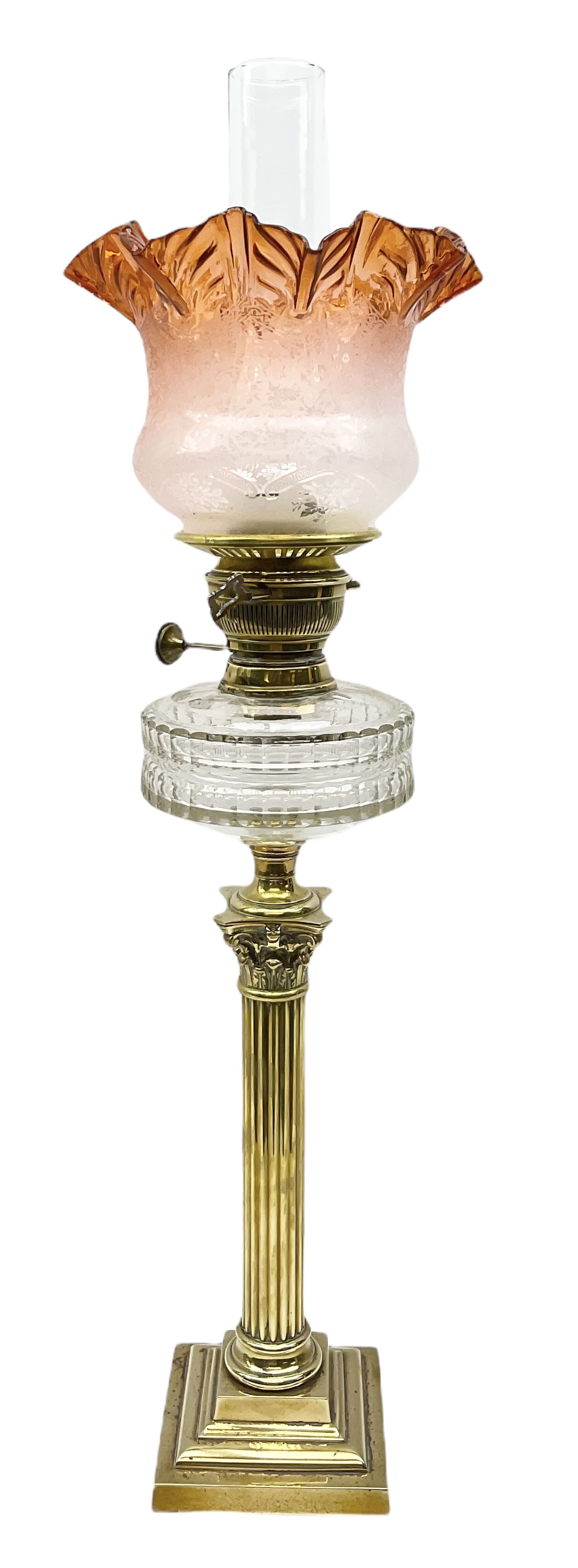 Victorian brass oil lamp, the square stepped base leading to a Corinthian column supporting a part slice cut clear glass reservoir, burner, clear glass chimney and foliate etched glass shade with amber rim, overall H80cm