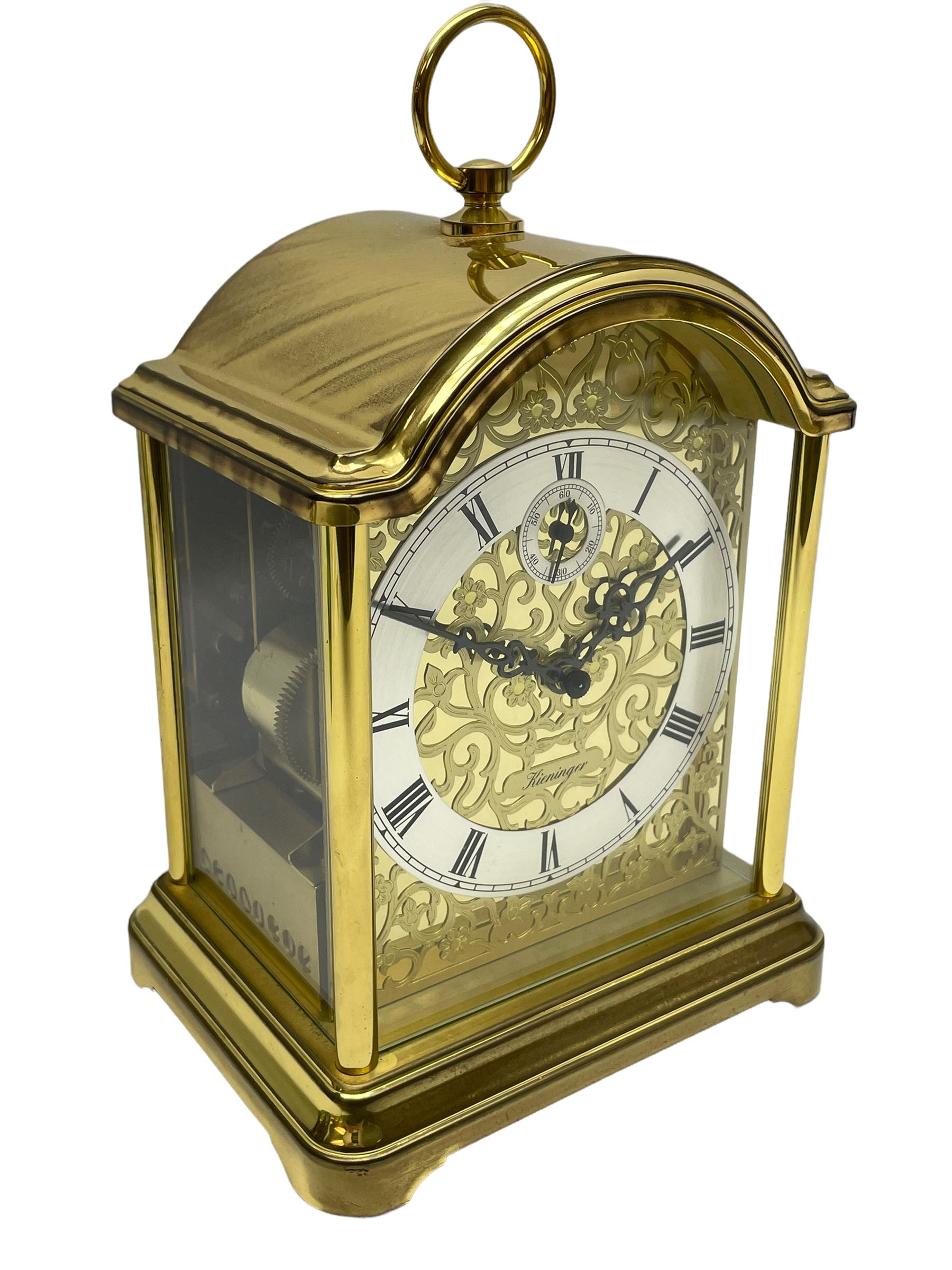 A 20th century brass cased Kieninger (German) chiming mantle clock with a break arch top and three glazed panels, polished sheet brass dial with applied  brass fretwork and a silvered chapter ring, Roman numerals, minute track, steel serpentine hands and seconds dial, three-train spring driven 8-day movement with Westminster, St Michael and Whittington chimes on 8 gong rods, 9 jewel lever platform escapement.  With key. 