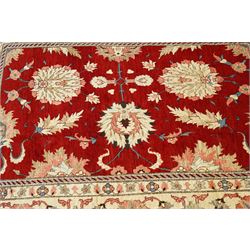West Persian Sarough hand-knotted carpet, rich madder red field, decorated with stylized palmettes angular vinery and floral sprays within multiple borders of ivory ground and scrolling foliate decoration, with cotton fringe ends 