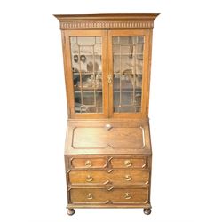 Early 20th century oak bookcase on bureau, projecting cornice with arcade carved frieze, two astragal  glazed doors enclosing three adjustable shelves, bottom section with fall-front top concealing pigeonholes and drawer, two short and two long drawers with panelled fronts, on bun feet