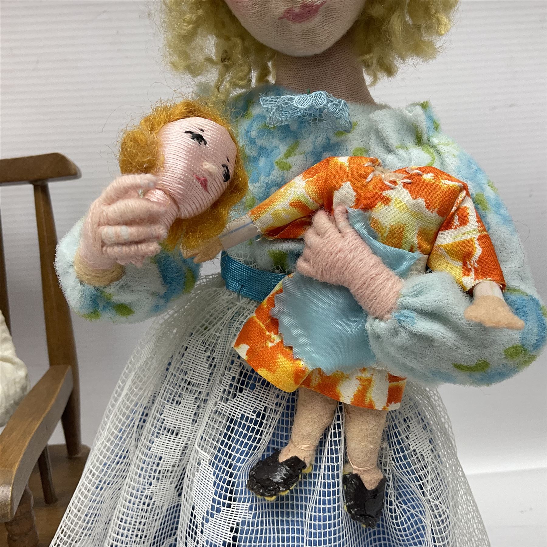 Anna Meszaros Hungary - three hand made needlework figurines - 'The Cobbler' as a child seated in a wooden rocking chair working on a removed boot H24cm; young girl standing crying holding a doll with broken head H32cm; and young girl in long dress and bonnet standing holding a doll H27cm (3)  Auctioneer's Note: Anna Meszaros came to England from her native Hungary in 1959 to marry an English businessman she met while demonstrating her art at the 1958 Brussels Exhibition. Shortly before she left for England she was awarded the title of Folk Artist Master by the Hungarian Government. Anna was a gifted painter of mainly portraits and sculptress before starting to make her figurines which are completely hand made and unique, each with a character and expression of its own. The hands, feet and face are sculptured by layering the material and pulling the features into place with needle and thread. She died in Hull in 1998.