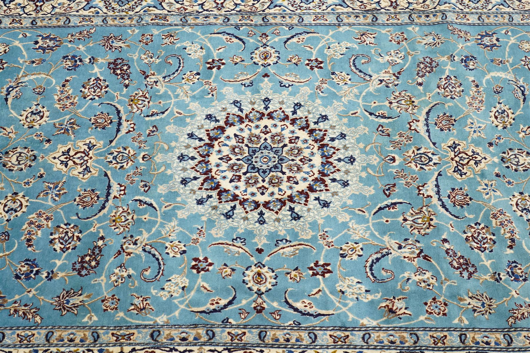 Central Persian Nain hand-knotted carpet, soft sky blue ground with central cusped medallion of radiating palmette form, issuing scrolling vine work, arabesques, and delicate floral sprays, spandrels of conforming design, main border of ivory ground decorated with scrolling vine work palmettes and stylized floral motifs, flanked by narrow guard stripes, with cotton fringe ends 