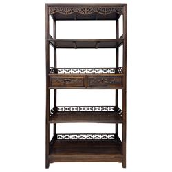Early 20th century Chinese hardwood display étagère bookcase, the rectangular open tiered frame with pierced frieze and geometric openwork gallery to each shelf, fitted with two short drawers carved with stylised lotus motifs, supported on square uprights with pierced apron and integral gallery rails