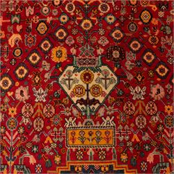 North Persian crimson ground rug, the field densely decorated with stylised flowering plants, urns and polychrome rosettes, within a stepped ochre outline, dark ground floral spandrels and geometric side panels