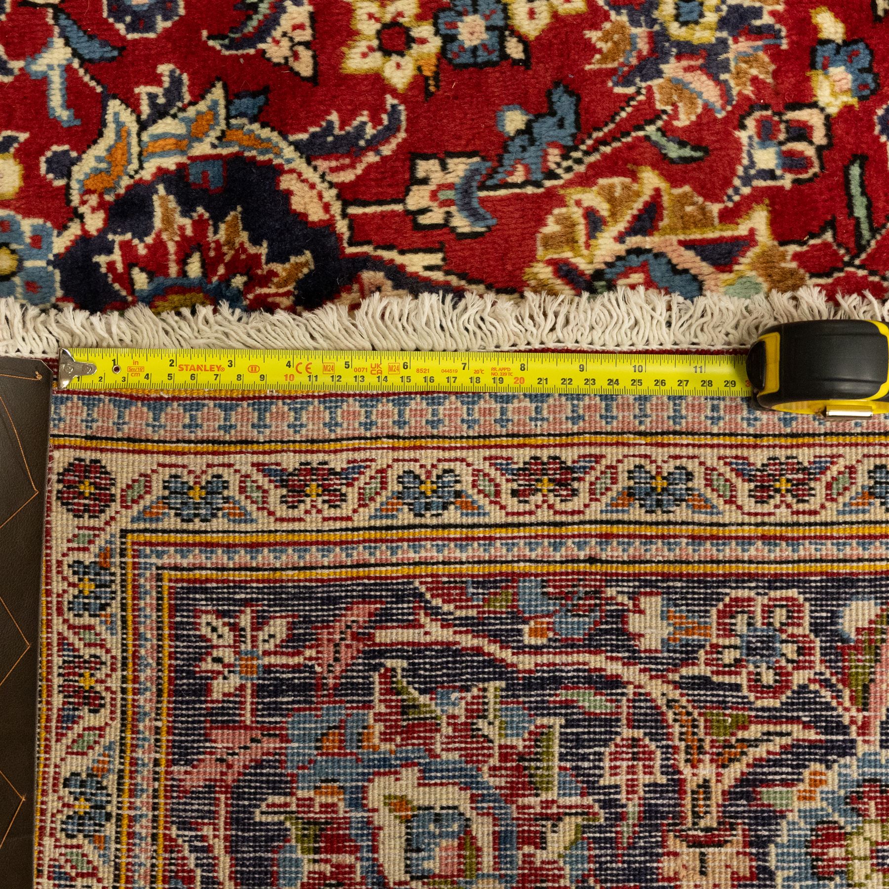 Central Persian Kashan hand-knotted carpet, crimson red central field with central floral medallion with floral vine-work and palmettes, within dense floral spandrels and a wide navy blue border decorated with continuous foliate motifs and multiple guard borders, with cotton fringe ends  