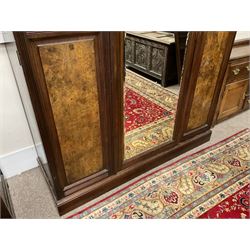 Late Victorian walnut triple wardrobe, the pierced broken swan neck pediment carved with foliate C-scrolls, central bevelled mirror door flanked by two panelled doors, the panels carved with urns, C-scrolls and trailing foliage, the interior fitted with hanging rails, long and short drawer, on moulded plinth base