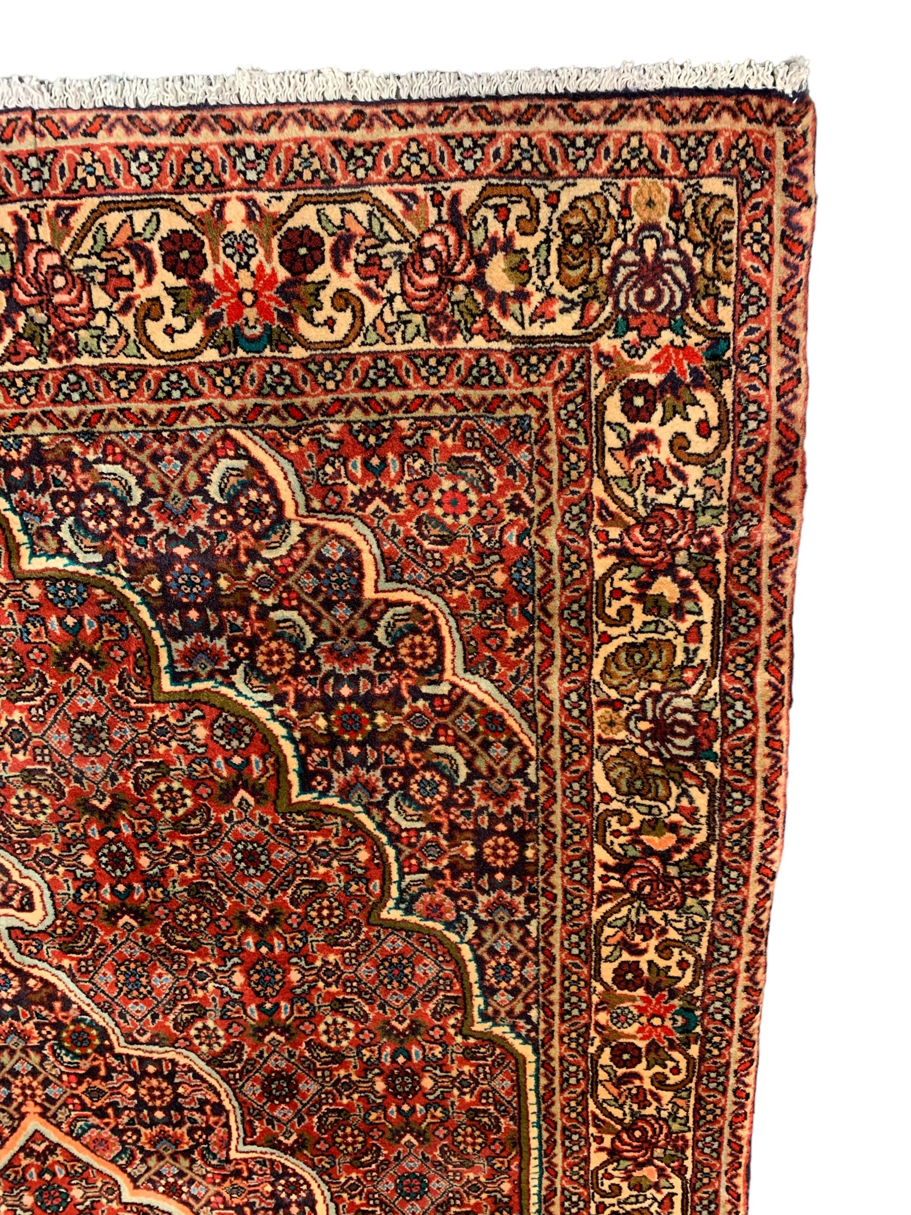 Persian Bidjar crimson ground rug, thick woollen pile, the field decorated with repeating Herati motifs within cusped outlines, the guarded border decorated with repeating flower head motifs
