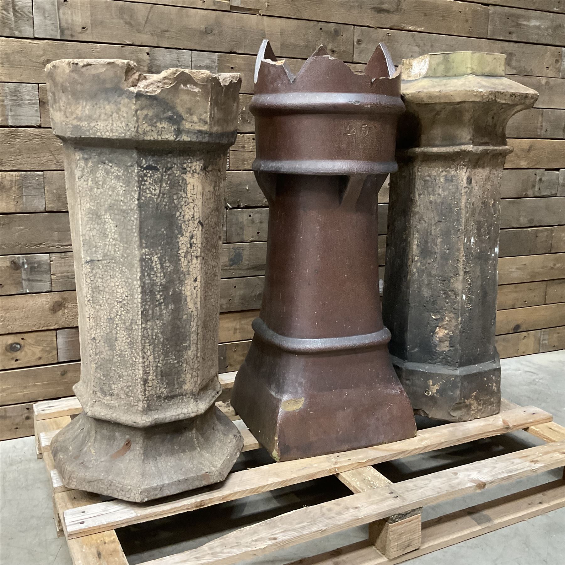 Collection of three Victorian and early 20th century reclaimed terracotta chimney pots, comprising: one cylindrical form with weathered, cracked glaze and flared octagonal base; one deep red cylindrical pot with fluted midsection and castellated rim, bearing moulded number ‘25’; and one tapering hexagonal example with wide flared rim and weathered patina. All with age-related wear and chips, consistent with use and outdoor exposure. Plus a selection of cast stone pieces including fountain 