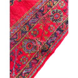 Early 20th century Western Anatolia Turkish Oushak crimson ground carpet, the field decorated with rows of Herati and Palmette medallions, the main border decorated with stylised flower head motifs within guard stripes