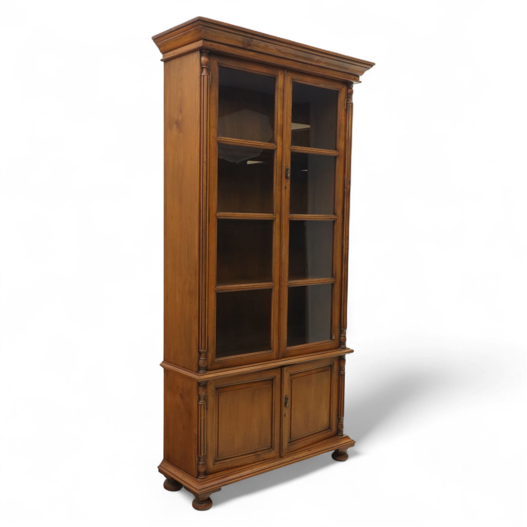 Pair of late 20th century Thai hardwood display cabinets, each with moulded cornice over twin glazed doors enclosing adjustable shelves, panelled cupboard doors below flanked by fluted columns, raised on bun feet