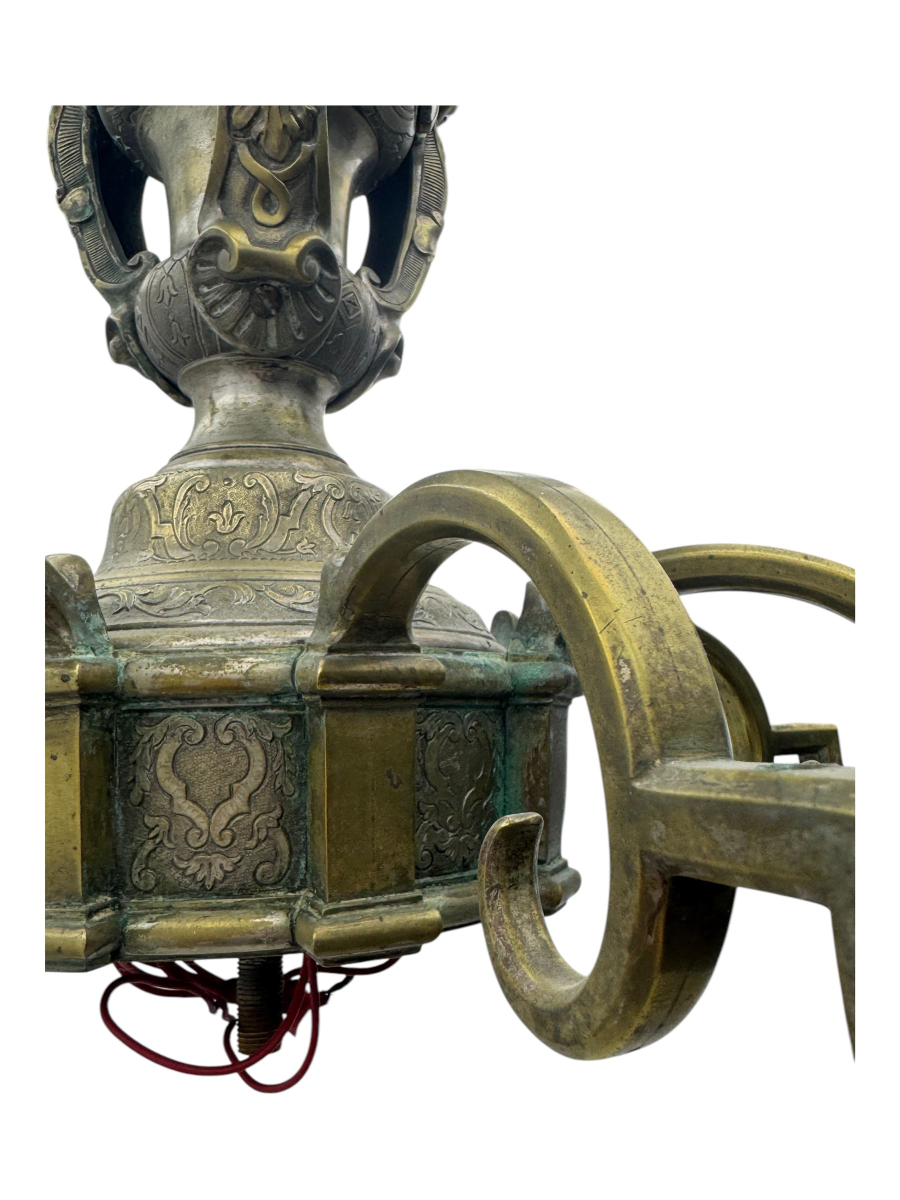 Early 20th century cast brass chandelier, the main baluster-form body surmounted by a lobed finial, with three cherubic heads and foliate scrollwork around the upper section, eight sweeping branches for lights