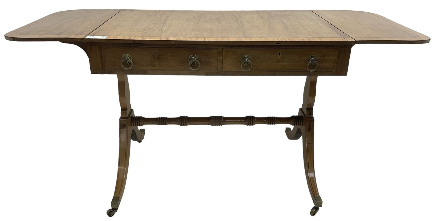 Regency mahogany sofa table, rectangular crossbanded top with twin drop-leaf ends, fitted with single drawer and one faux drawer, raised on shaped end supports united by ring turned stretcher