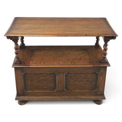 Early 20th century oak monks bench, panelled back converting to a table top, reeded armrests with barley twist uprights, hinged seat over panelled base supported on bun feet