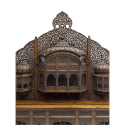 Late 19th century Indian Burmese carved and pierced hardwood and brass inlaid wall shelf, the shaped back profusely decorated with trailing and interlaced foliage, with projecting architectural structures, the central balcony with canopy top and five open windows with arched apertures on columns, two flanking five-sided balconies, the shelf supported by six foliate carved columns with pierced cusped pointed arches 