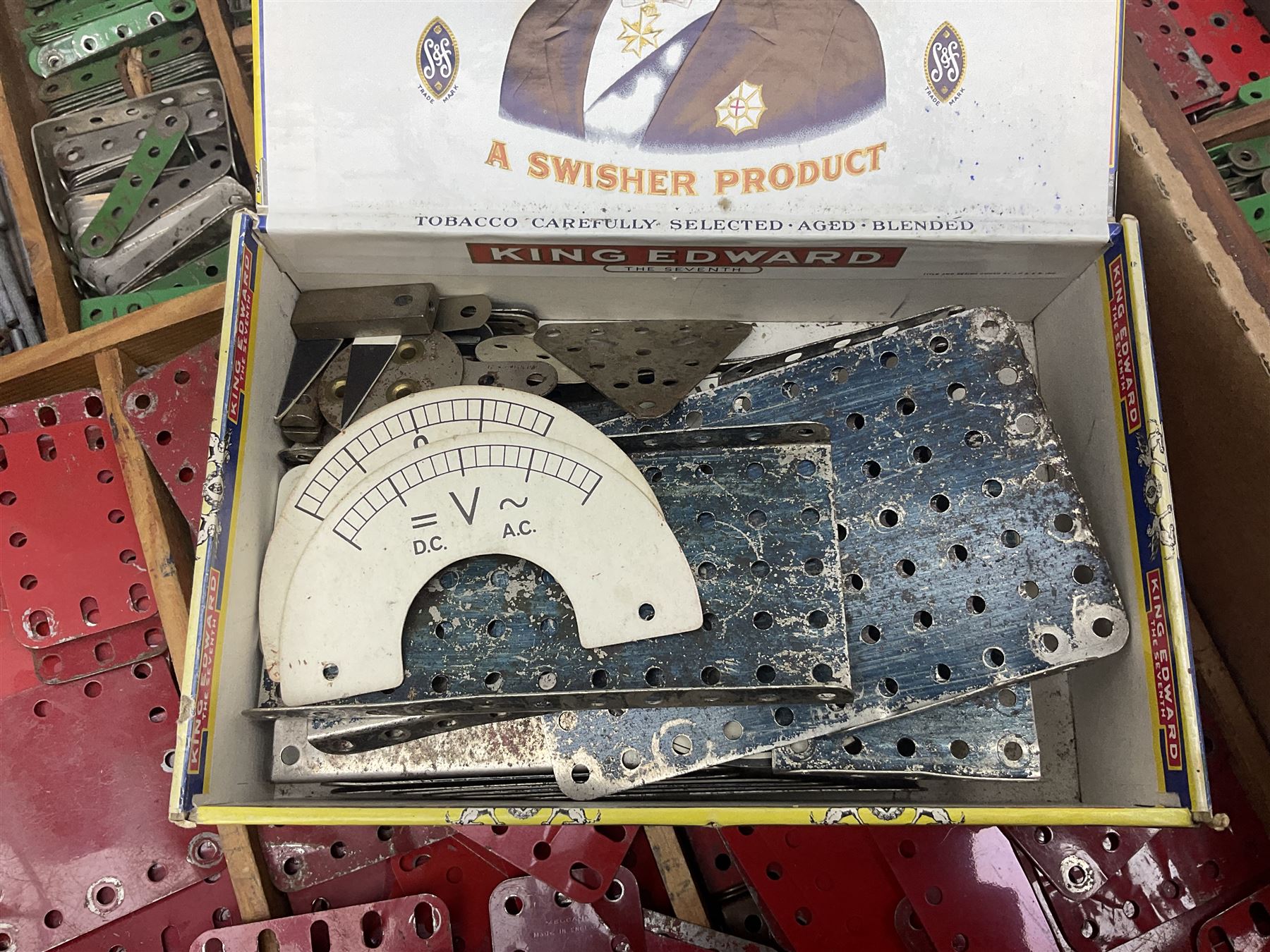 Meccano - large quantity of loose parts including various plates and strips, flanged plates, pulleys, axle rods and crank handles, wheels and tyres, gear wheels, brackets, nuts & bolts, various manuals; predominantly red and green; some in compartmentalised wooden trays