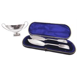 Victorian silver salt, of navette form with twin curved handles, engraved floral swag, and beaded rim, upon a spreading stem with conforming beaded edge, and rectangular base, hallmarked Henry Holland, London 1878, together with a pair of Victorian silver Fiddle pattern butter knives, hallmarked Hilliard & Thomason, Chester 1897, contained within a fitted case with blue silk and velvet lined interior, approximate total silver weight 5.35 ozt (166.5 grams)