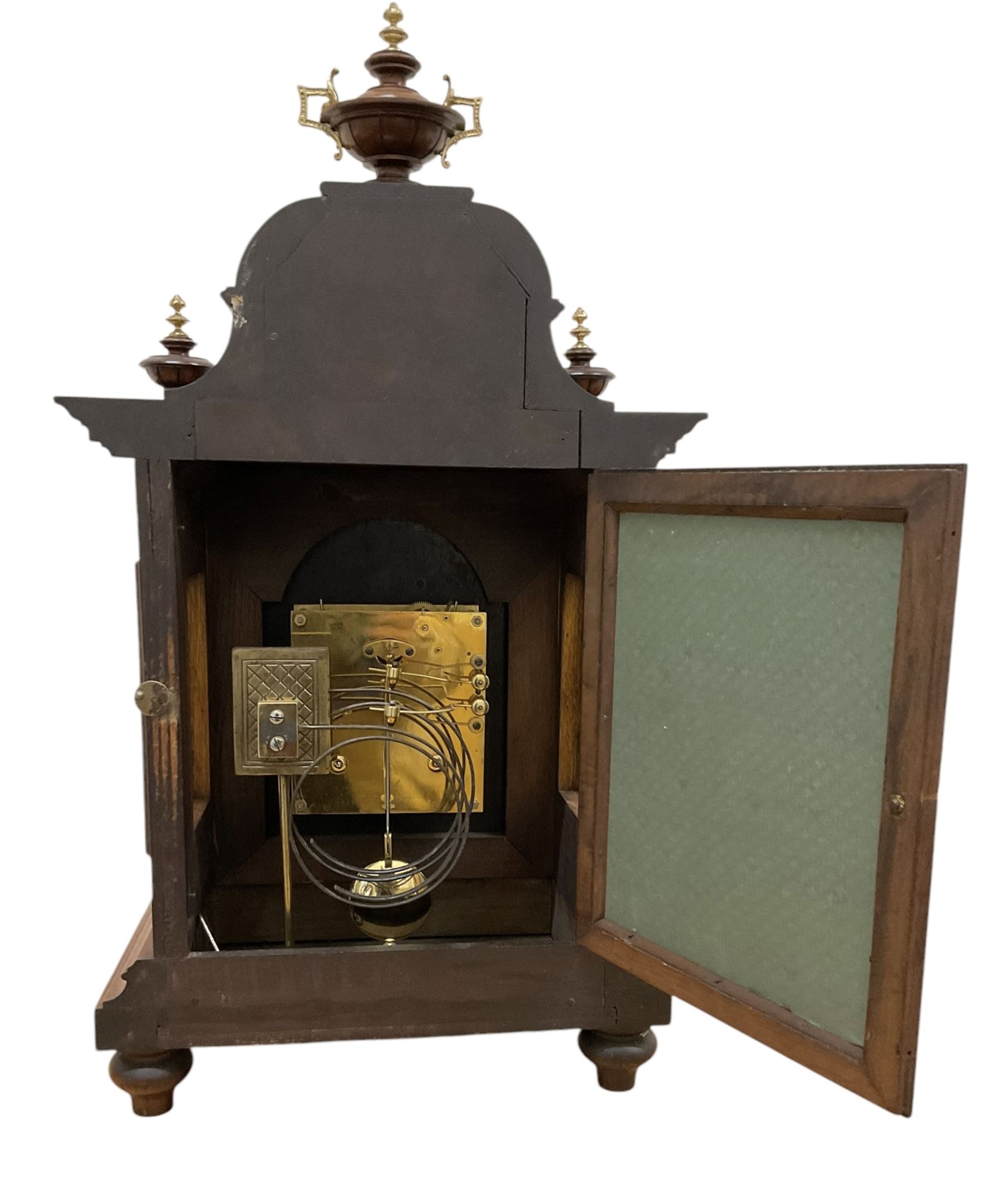 Junghans-German early 20th century walnut cased 8-day mantle clock, with an ogee carved pediment and turned wooden finials, break arch door with brass spandrels beneath flanked by brass caryatids, glazed panels to the sides on a stepped plinth raised on  brass paw feet,  brass dial with a matted centre and silvered chapter with Arabic numerals and Fleur-di Lis steel hands, twin train rack striking movement with a ting tang chime on the quarters. With Key and pendulum. 