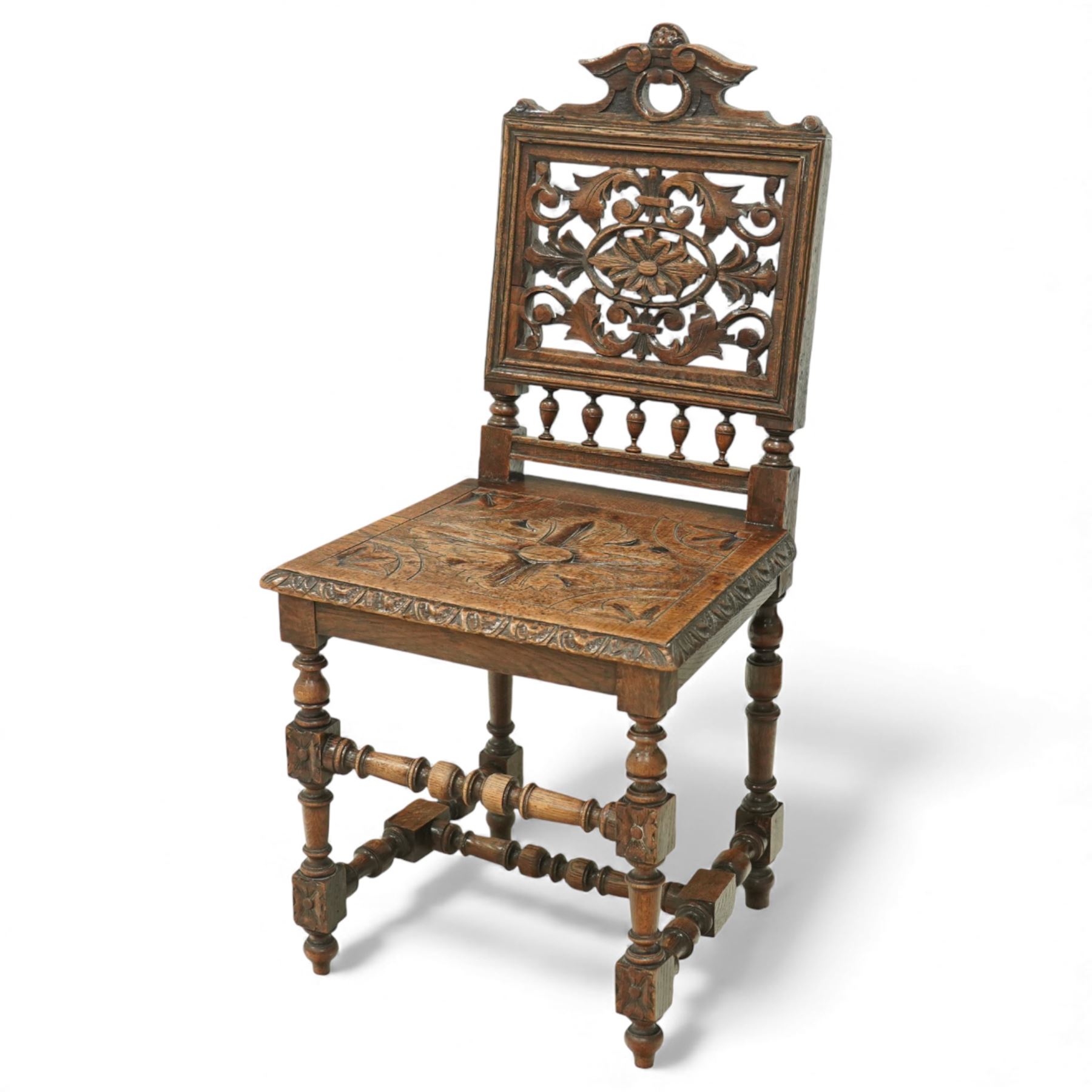 18th century carved oak hall chair, the rectangular pierced back carved with scrolling foliate ornament and central rosette beneath a shaped cresting, the boarded seat carved with stylised foliage, raised on turned legs united by stretchers
