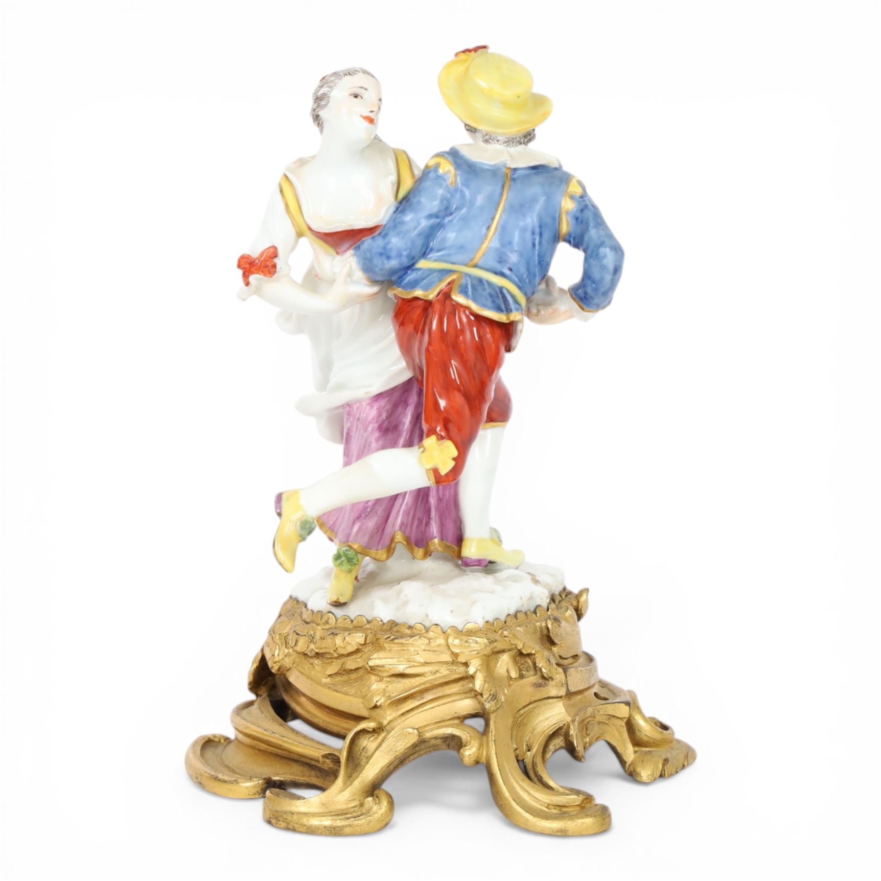 Mid 18th century Meissen figure group, The Tyrolean Dancers, circa 1740, modelled as two swirling figures with their arms linked, he in yellow hat with red rosette, blue jacket, red breeches with red rosette, and yellow shoes with green rosette, she in white blouse with red ribbons, yellow and red bodice, white apron over puce skirt and yellow shoes with green rosettes, her hair fashioned into two plaits secured by red ribbon, upon a shaped mound base, within a scrolling gilt metal mount, with blue crossed swords mark to base, overall H19cm
