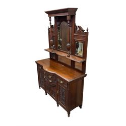 Edwardian walnut sideboard, projecting cornice supported by turned supports, the back fitted with three bevelled mirrors beneath fluted and flowerhead carved friezes, the lower section with four drawers and four panelled cupboard doors carved with foliate and urn designs, fluted uprights on turned feet