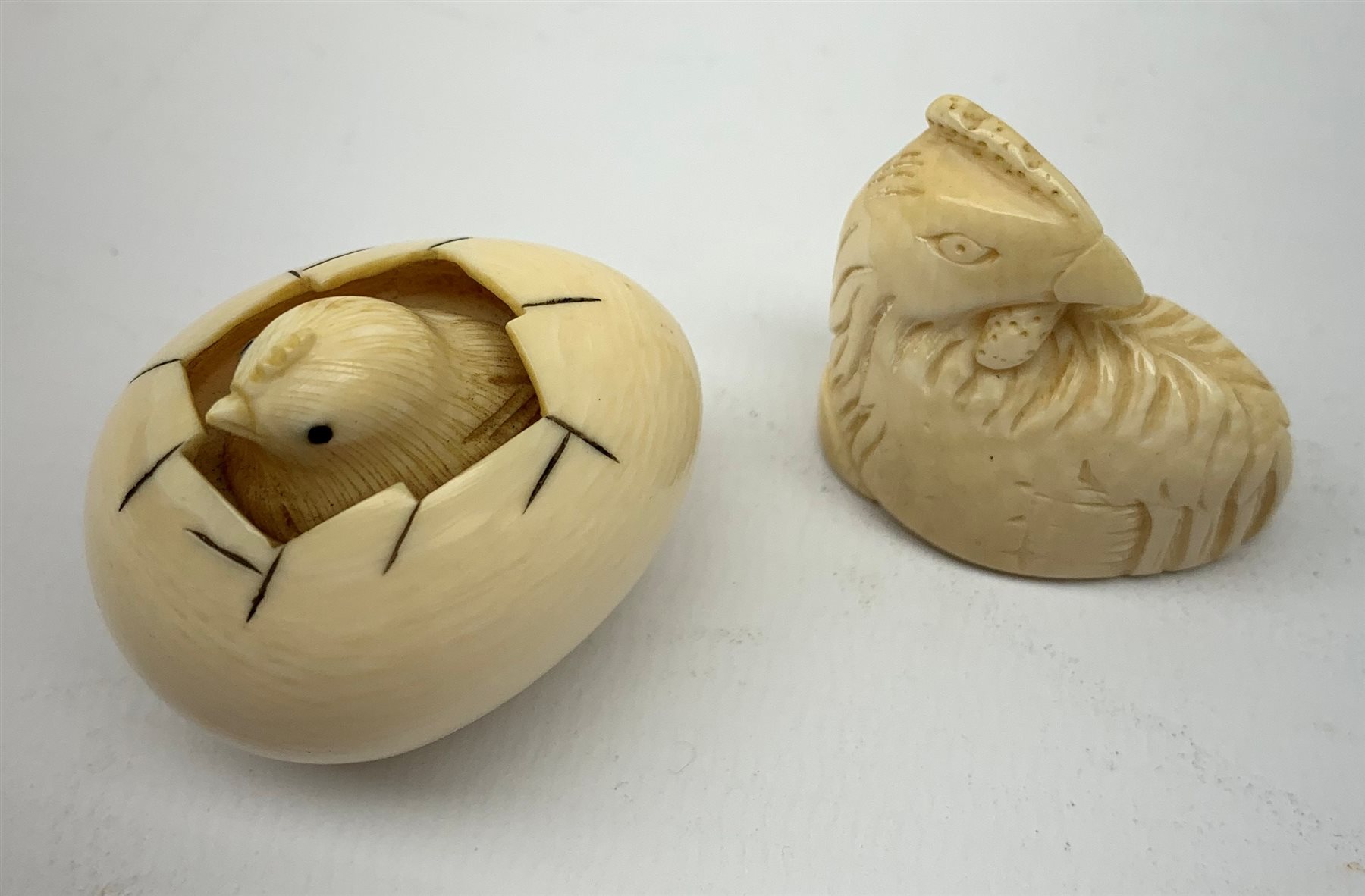 A Japanese ivory netsky modelled as a chick hatching from an egg, with marks beneath, together with a further netsky modelled as a seated chicken, also marked, a carved ivory cheroot holder, and two small carved ivory elephants, plus a Japanese stand modelled in the form of a crane, with character marks to base, a Japanese bamboo detailed teapot, cloisonne circular  pot, and an embroidered pouch and purse. 
