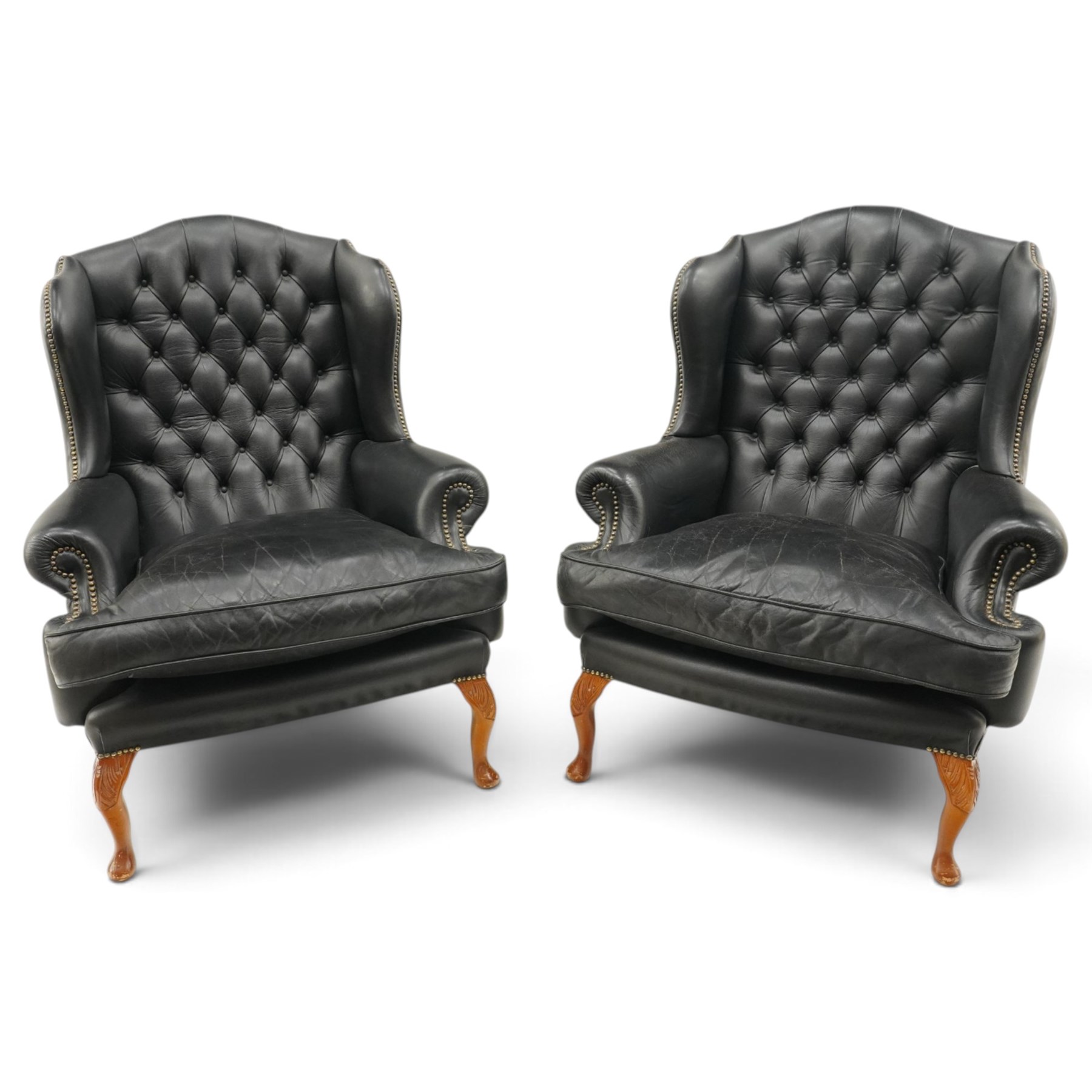 Pair of quality Georgian design wingback club armchairs, the high arched back with wings over rolled arms, upholstered in back-buttoned black leather with loose seat cushion, raised on foliate carved cabriole supports