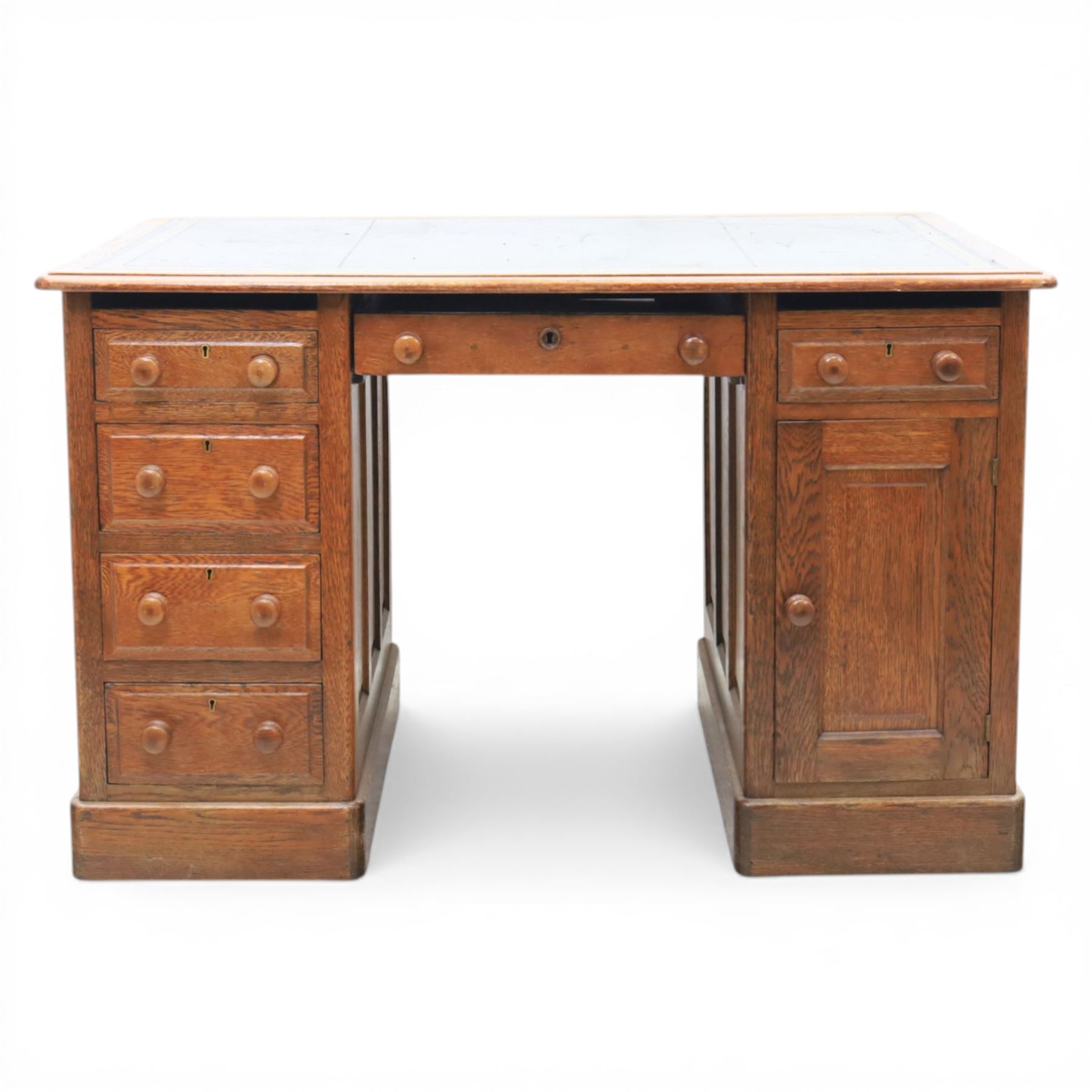 20th century oak compact pedestal desk, tooled green leather inset top, above a single frieze drawer, with a bank of four graduated drawers and a drawer and cupboard, panelled sides raised on castors