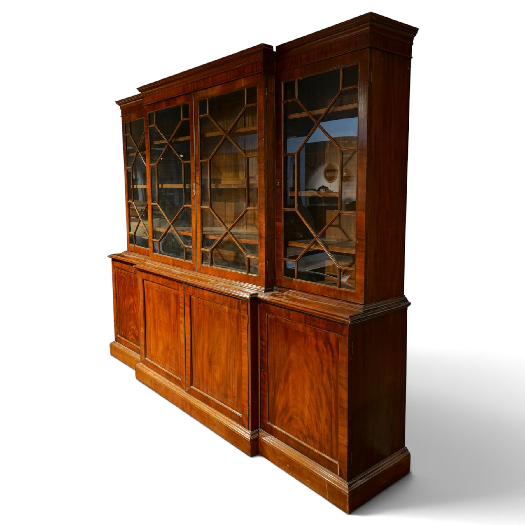 Fine Regency mahogany breakfront library bookcase, the stepped and moulded cornice over four astragal glazed doors enclosing adjustable shelves, the projecting central lower section with a pair of panelled doors enclosing three graduated drawers with brass inset handles above two deep zinc-lined cellarette compartments, flanked by panelled cupboard doors enclosing shelves, the figured mahogany fronts with ebony line inlay, on moulded plinth bases