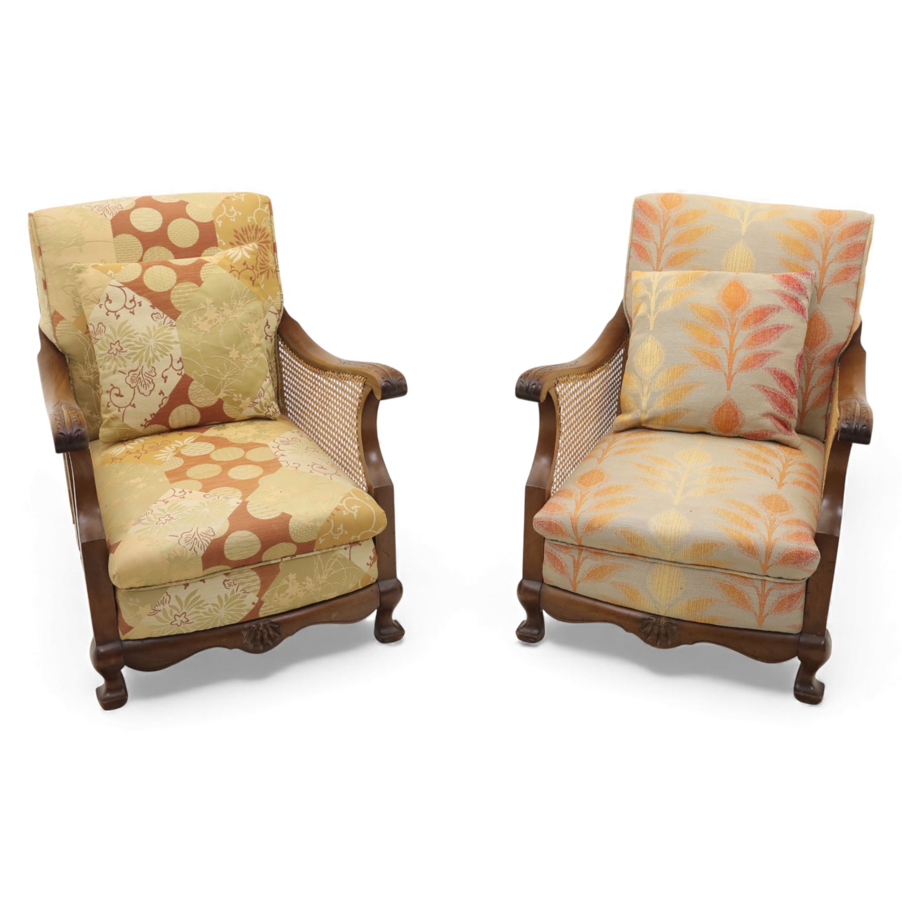 Pair of mid-20th century mahogany framed bergère armchairs, each with carved scroll arms and caned side panels, floral upholstered loose cushions, raised on cabriole front supports