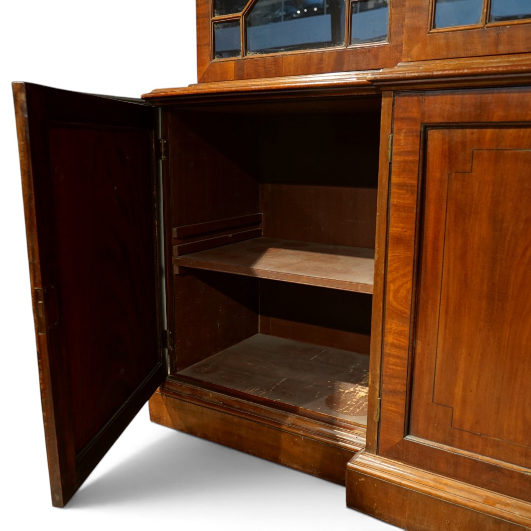Fine Regency mahogany breakfront library bookcase, the stepped and moulded cornice over four astragal glazed doors enclosing adjustable shelves, the projecting central lower section with a pair of panelled doors enclosing three graduated drawers with brass inset handles above two deep zinc-lined cellarette compartments, flanked by panelled cupboard doors enclosing shelves, the figured mahogany fronts with ebony line inlay, on moulded plinth bases