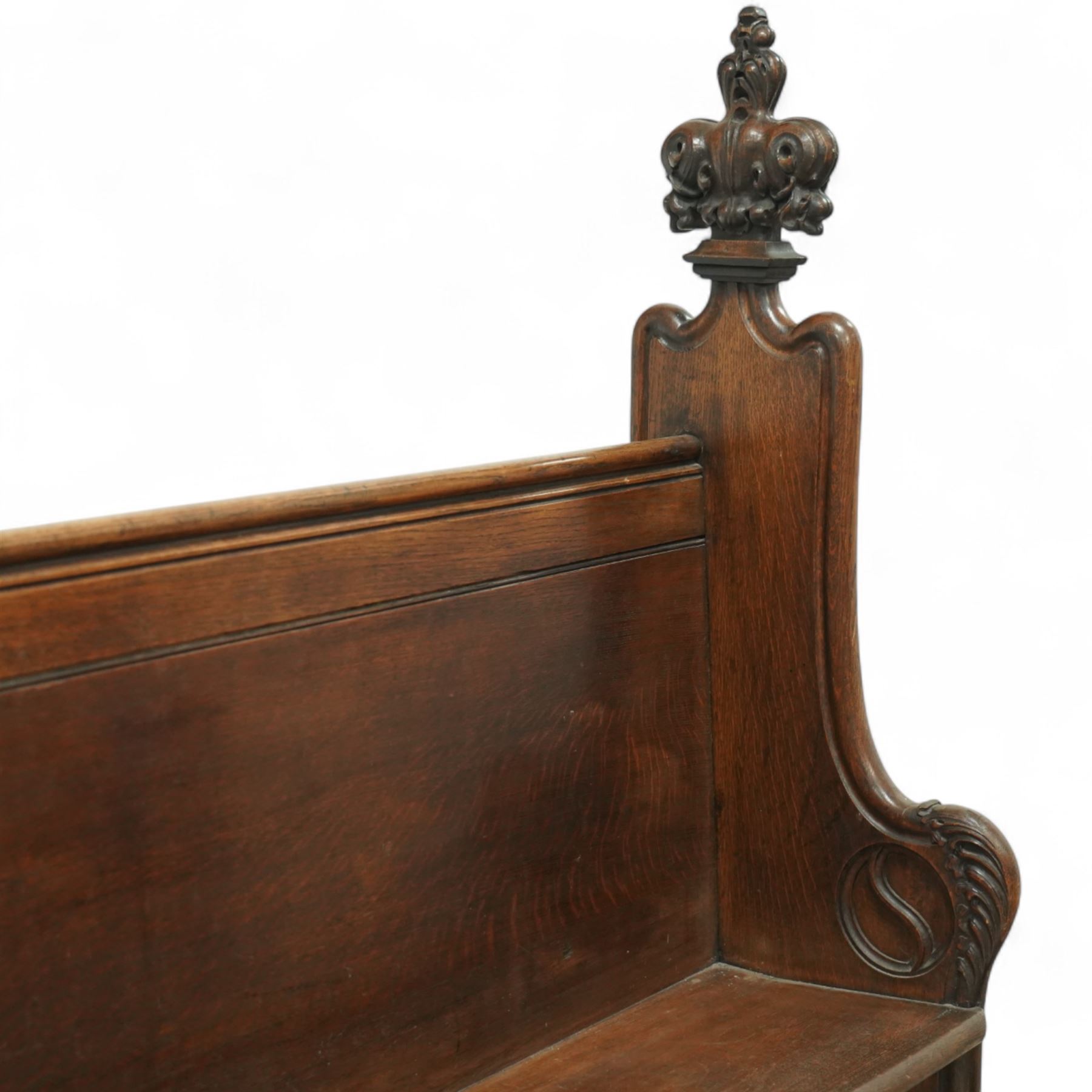 Late 19th century Gothic revival oak church pew, with high backrest framed by carved stylised cross panels and crown-topped finials, shaped end panels with scroll detailing, on block end supports and central stretcher, with later padded seat cushion
