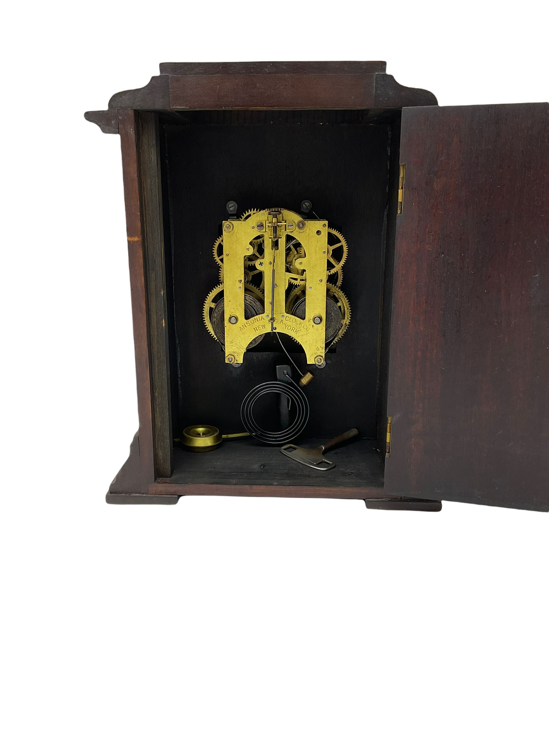 An American Mantle clock in a mahogany case with an eight-day “Ansonia” striking movement, case with a flat top and reeded pillars on a broad plinth with raised feet, square engraved and silvered dial with roman numerals and minute track, steel spade hands and pendulum regulation, sounding the hours and half hours on a coiled gong. With pendulum and key.  






