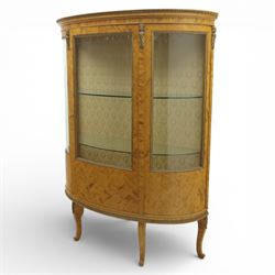 Edwardian satin walnut display cabinet, bowed oval form with moulded and dentil cornice over glazed panels, enclosing a laurel wreath damask interior with adjustable glass shelves, the frame applied with gilt metal bead mouldings and mask mounts, enclosing a shelved interior, raised on cabriole supports with moulded feet
