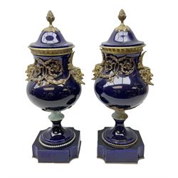 Pair of French large cobalt blue lidded urns, probably 19th century, the body decorated with ormolu ram's heads and ornate foliate design, the domed cover with brass berry finial, raised upon pedestal base with beaded decoration upon shaped plinth, H52cm