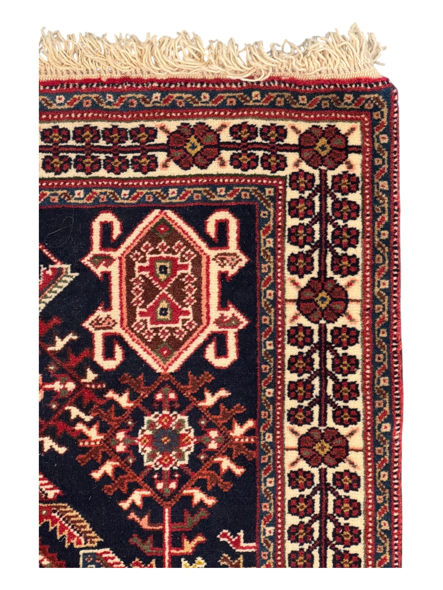 Persian Qashqai crimson ground runner, the central field decorated with three large geometric medallions with intricate angular and floral motifs, the indigo spandrels with complementary geometric designs, bordered by an ivory band with repeating floral patterns and angular vines