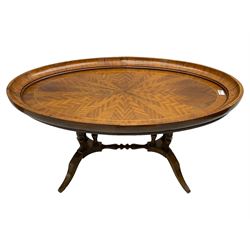 Early 20th century walnut coffee table, oval dished top with sunburst matched veneer, raised on twin cluster columns united by turned stretcher base on splayed supports