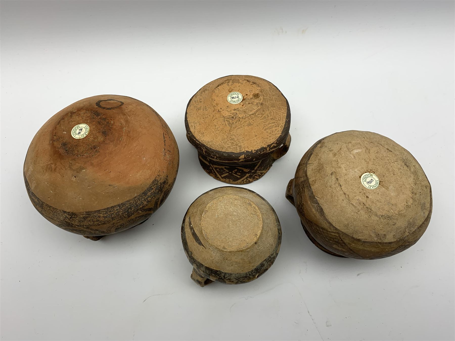 Four Chinese Neolithic pottery vessels, each with twin loop handles to the shoulder and painted geometric banded decoration to the body, three bearing labels for Eskenazi London, tallest H13cm