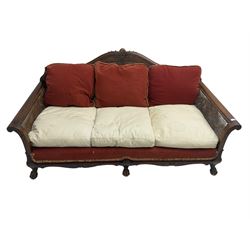 Early 20th century bergère three seat settee, shaped shell carved cresting rail, double caned back and sides, scrolled upright arms and shaped apron carved with shell and foliage, on hairy paw carved feet