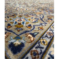 Central Persian Kashan hand-knotted carpet, the ivory ground intricately decorated with scrolling vines, palmettes, and stylised flowerheads in soft blue, gold and brown tones, enclosed by a broad indigo border with repeating floral motifs and multiple guard stripes