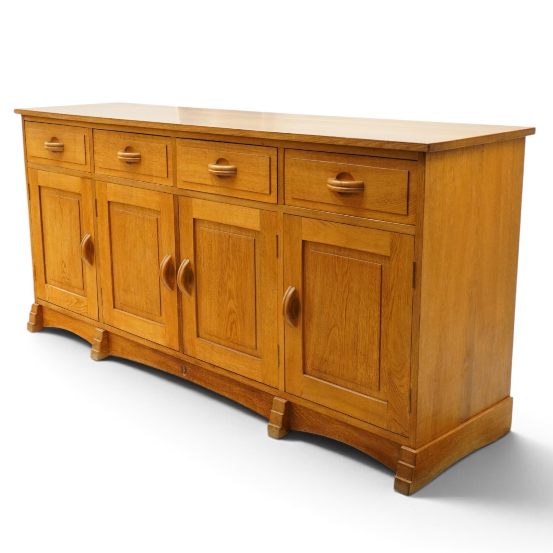 Acorn Industries - oak dresser base or sideboard, the rectangular top over three drawers with protruding oak handles, over four panelled cupboard doors enclosing a single shelf, raised on stepped feet, carved with acorn signature, by Alan Grainger, Brandsby