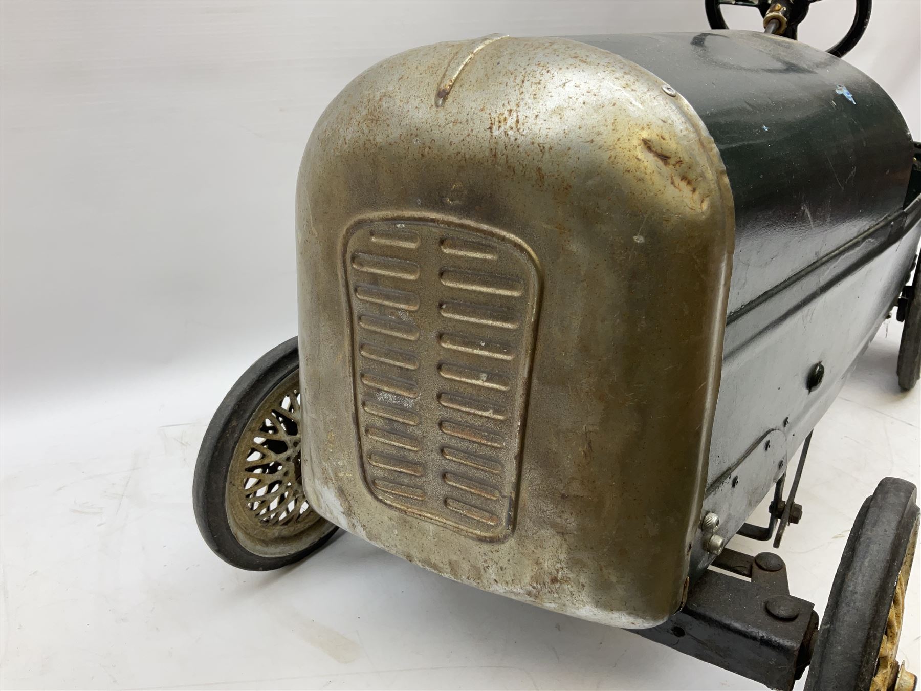 Mid 20th century pressed steel pedal car, the body painted in dark green fitted with pretend radiator to the bonnet, with spoked wheels and rubber tyres, the interior with pedals and steering wheel, L70cm